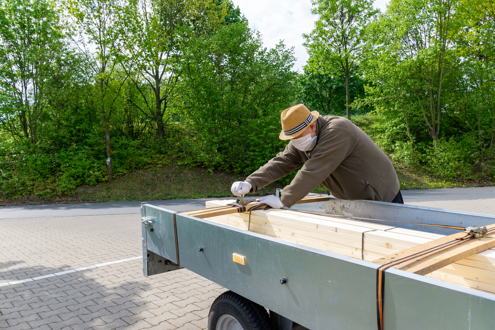Fotografi av en eldre mann som sikrer lasten av planker på hengeren sin.